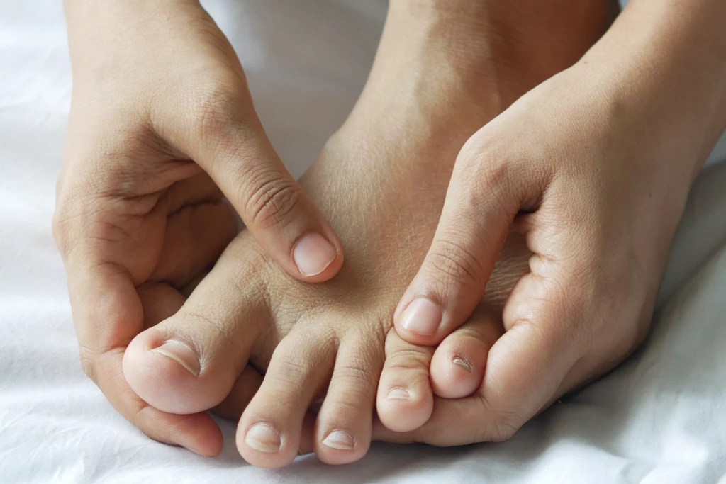 Both hands squeezing across the forefoot of a bare foot, the area between the lesser toes where Morton's neuroma causes nerve pain.