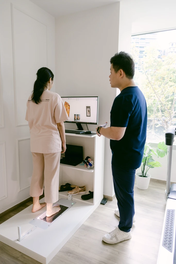 A patient standing barefoot on a foot scanner while a podiatrist reviews the image on a monitor, the forefoot loading assessment used when Morton's neuroma is suspected.