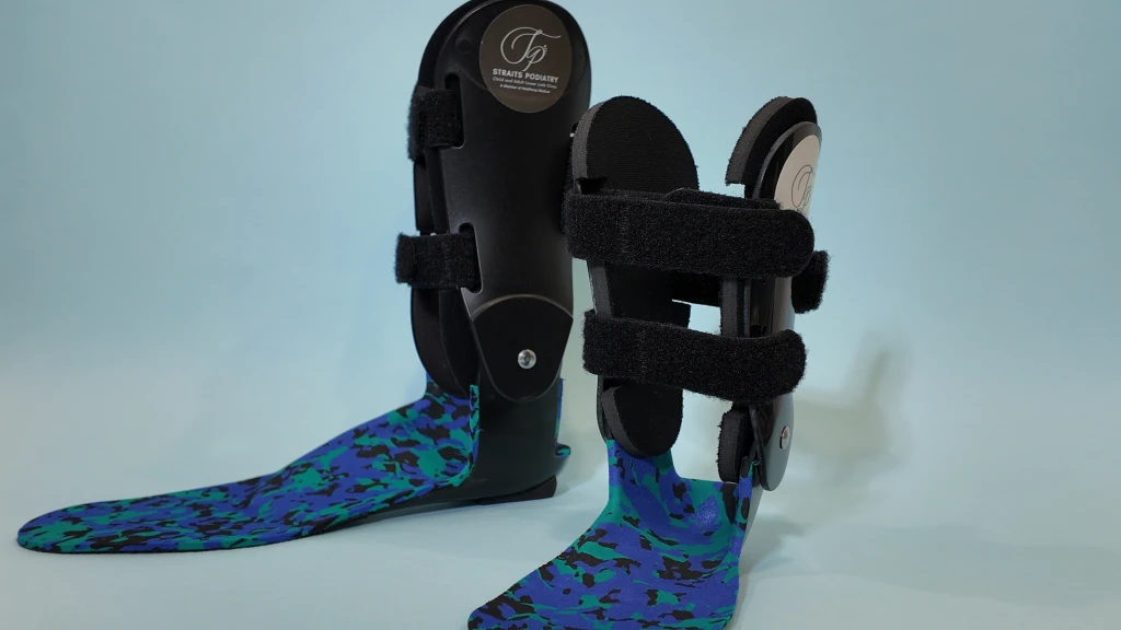 一对黑色定制踝足矫形器,配有魔术贴绑带和 Straits Podiatry 海峡足科标志,各自装有蓝色、青色与黑色迷彩花纹的模压足部内衬,置于淡蓝色背景前。