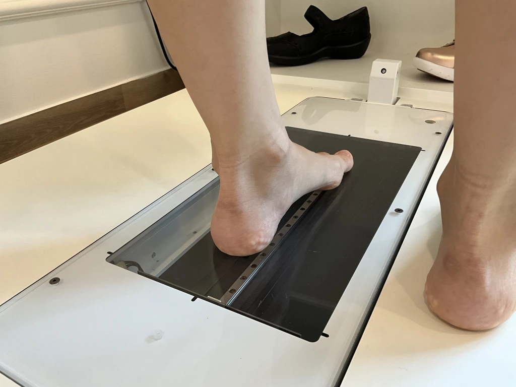 A patient's bare foot resting on a clinic foot scanner plate during a biomechanical assessment, the scan used to record arch shape and identify high arches.
