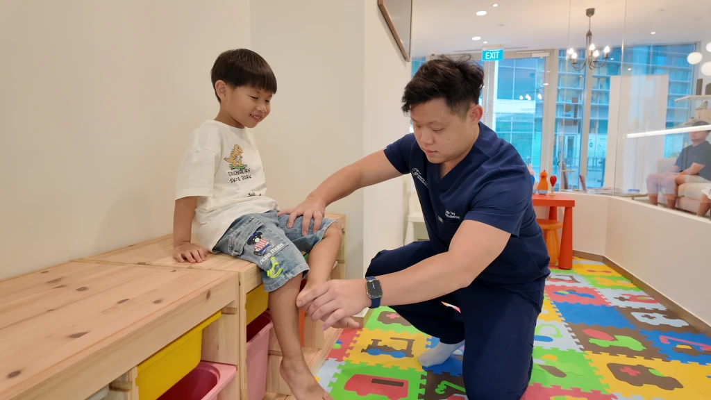 足科医师在诊所的儿童游乐区检查小男孩的足部,评估科勒病。