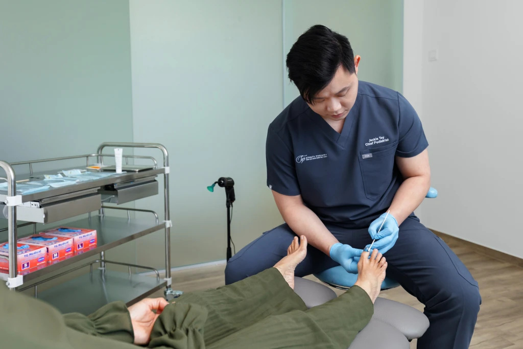 Straits Podiatry 海峡足科的足科医师在治疗椅旁用棉签涂抹患者的脚趾甲,进行 PACT 抗真菌治疗。