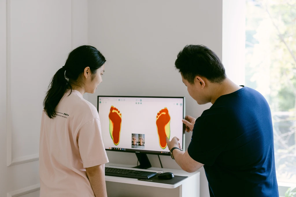 A podiatrist and a patient viewing a colour foot pressure scan on a monitor, the gait assessment used when tarsal tunnel syndrome is suspected.