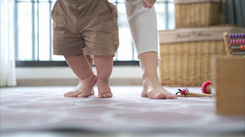 幼儿在游戏垫上赤脚迈出早期步伐,旁边有成人陪伴