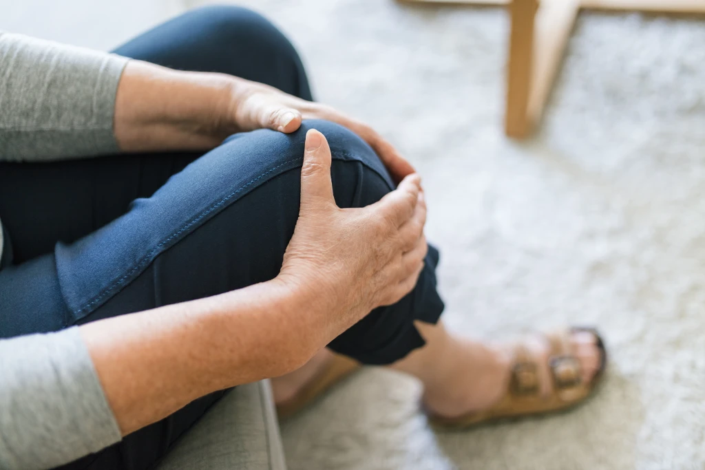 An older woman seated at home holding her knee, indicating knee pain