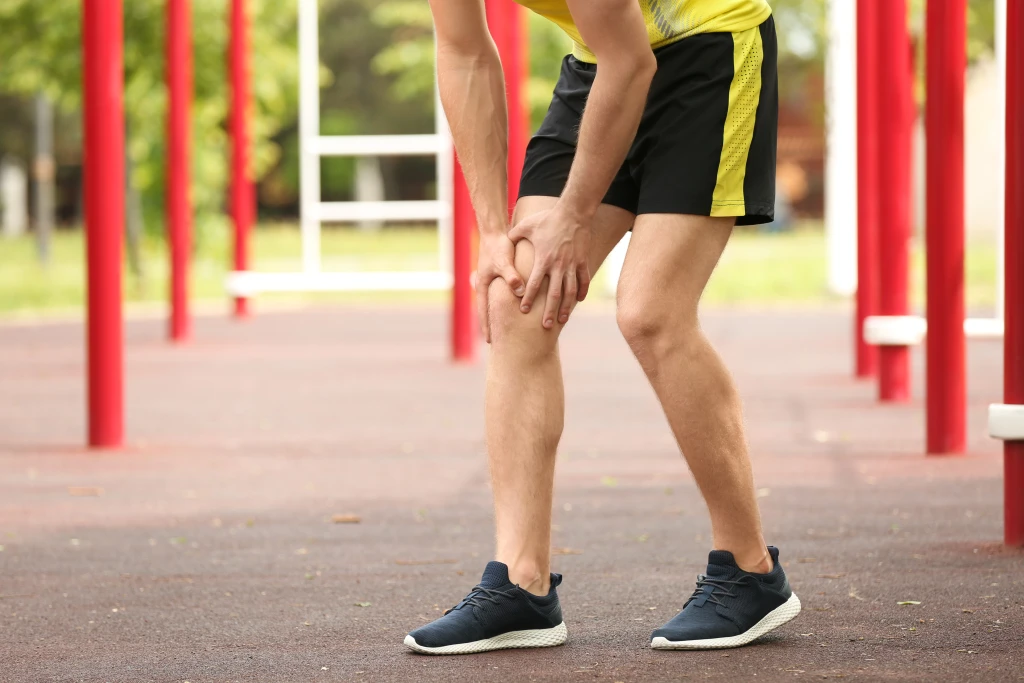 A man in sportswear holding his knee in pain while exercising outdoors