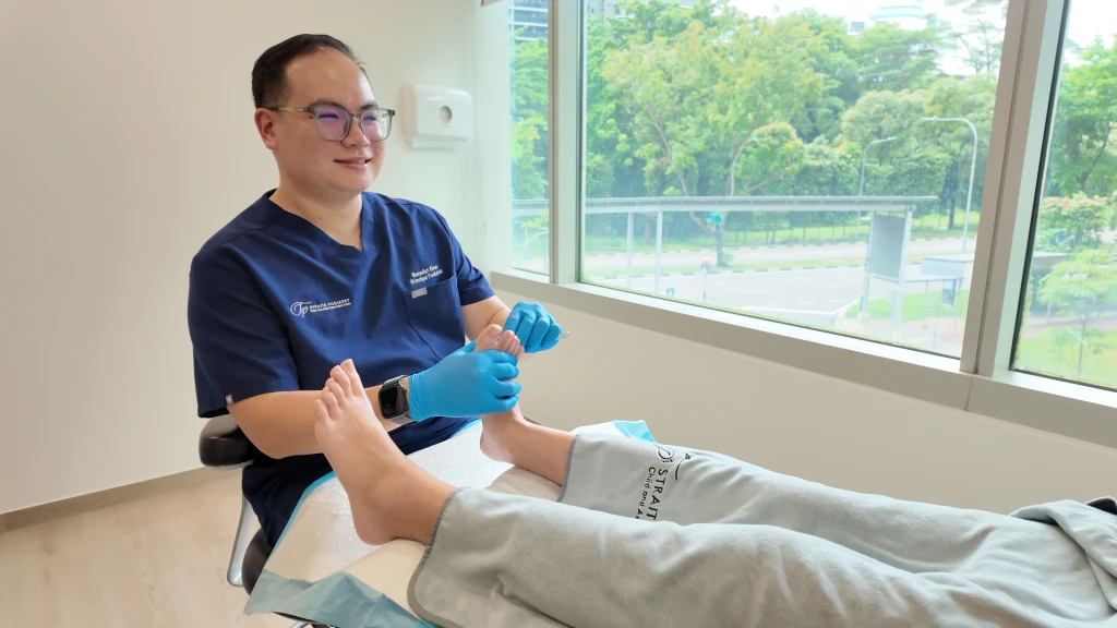 Straits Podiatry 海峡足科的足科医师身穿深蓝色制服并戴着淡紫色手套,托起并检查患者的足底。