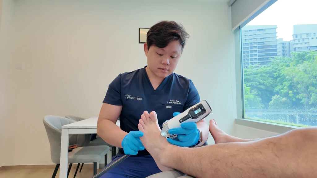 一位足科医师戴着蓝色手套，在诊疗室内将手持式治疗仪器施用于患者的足背。