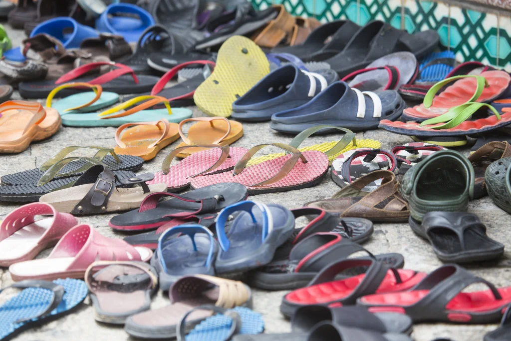 Dozens of assorted flip-flops, slides, and flat sandals laid out in rows, the thin unsupportive styles that aggravate plantar fasciitis.