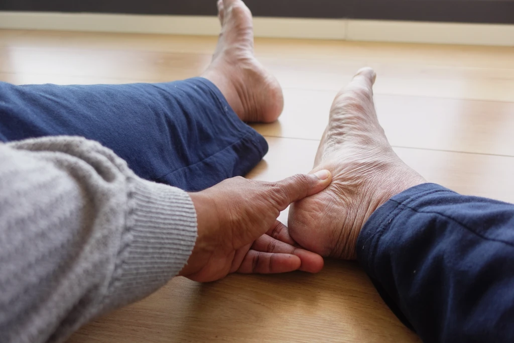 A person seated on the floor pressing a thumb into the arch and heel of one bare foot, locating the plantar fasciitis pain point.