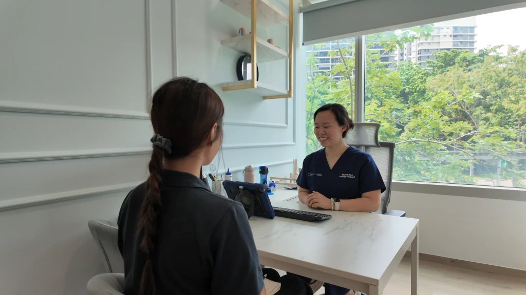 Straits Podiatry的足科医师坐在诊桌旁,在跟骨应力性骨折问诊中与患者讨论足跟疼痛。