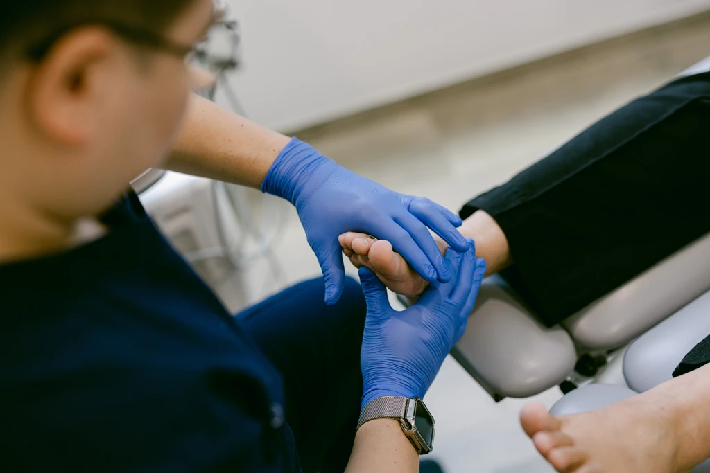 A Straits Podiatry podiatrist examining a patient's foot with gloved hands during a consultation.