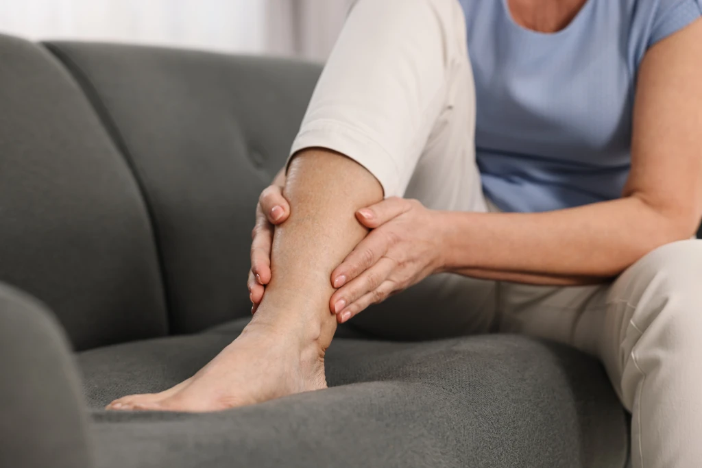 An older woman sitting on a sofa holding her lower leg and foot, indicating leg pain