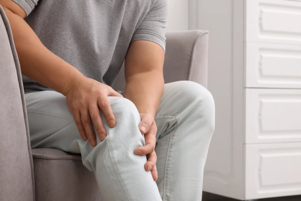A man sitting in a chair holding his knee, indicating leg pain