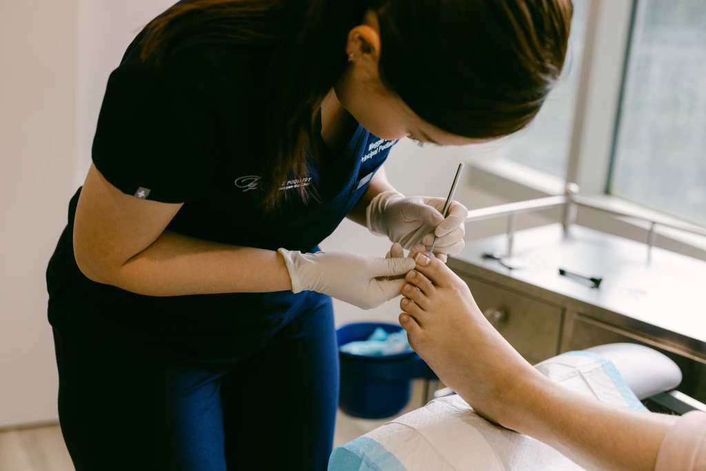 A Straits Podiatry podiatrist bending forward to work on a patient's big toenail with a fine instrument during a nail bracing appointment.