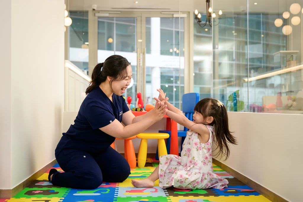 Ms Michelle Goh, Principal Podiatrist, sharing a high-five with a young child in the clinic's children's corner.