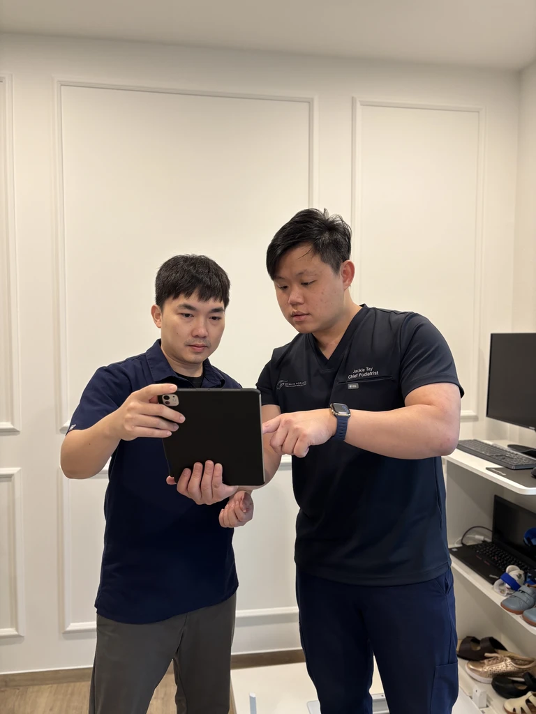 Physiotherapist Mr Chan Lai Jie and Chief Podiatrist Mr Jackie Tey reviewing a patient's assessment together on a tablet.