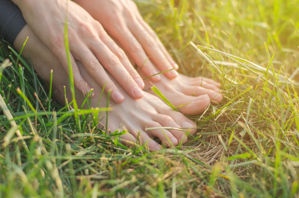 Bare feet and hands resting together on sunlit grass, the comfortable everyday feet that simple foot care tips aim to maintain.