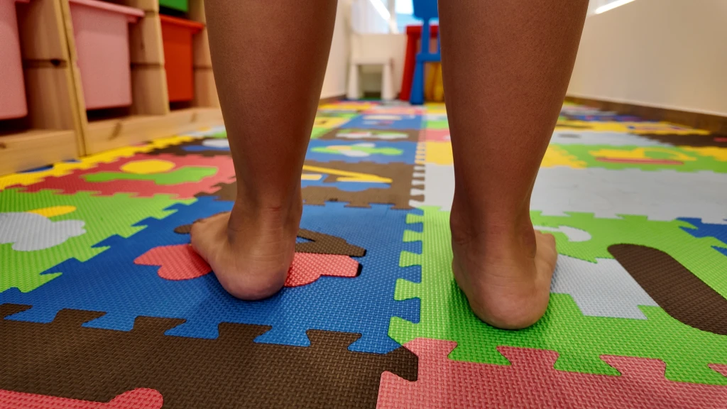 Rear view of bare feet and heels standing on a colourful foam play mat, the standing check from behind used in working out how to know if you have flat feet.