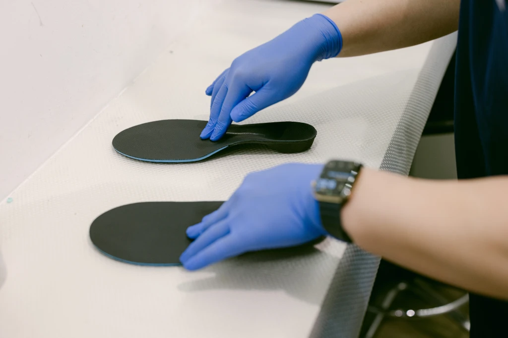 A clinician in blue gloves positions two black custom orthotic shells on a white workbench, the individually made devices at the centre of the orthotics vs insoles comparison.
