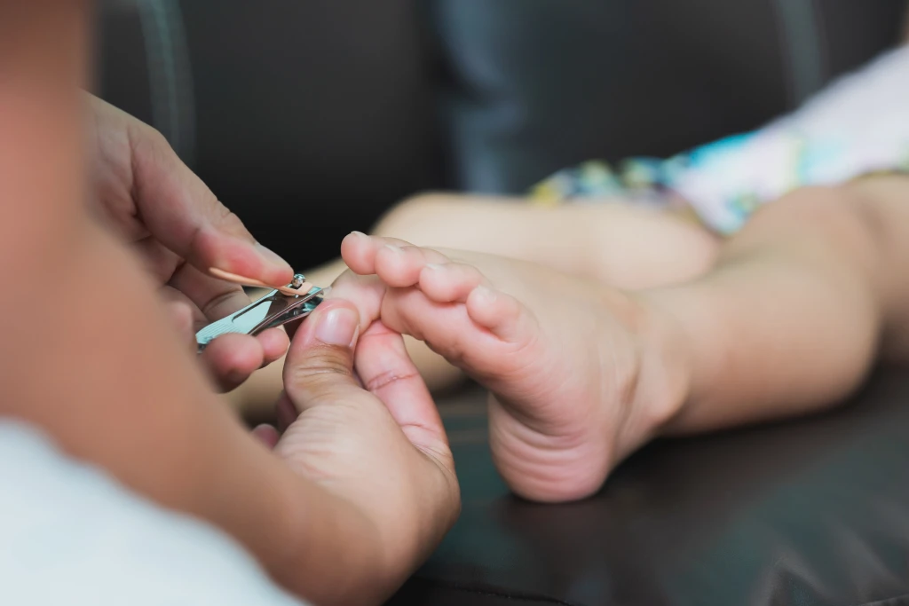 Close-up of an adult's hands using a small clipper to trim a child's toenail, the delicate nail care behind why ingrown toenails in children are treated differently.