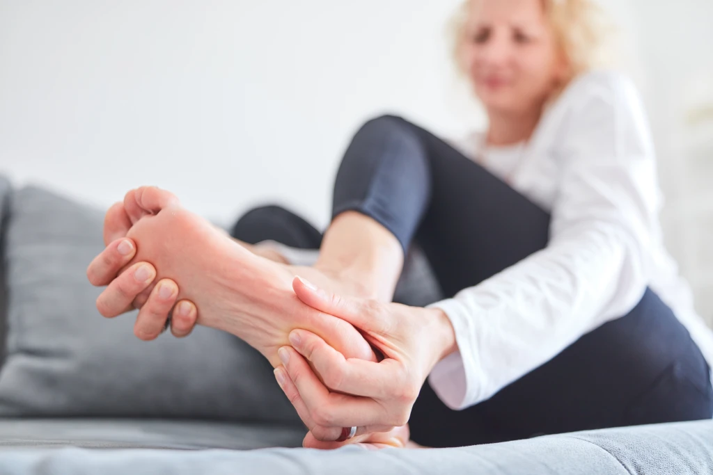 A person sitting on a sofa clasping the arch and heel of one bare foot with both hands, the lingering discomfort behind asking how long does plantar fasciitis take to heal.