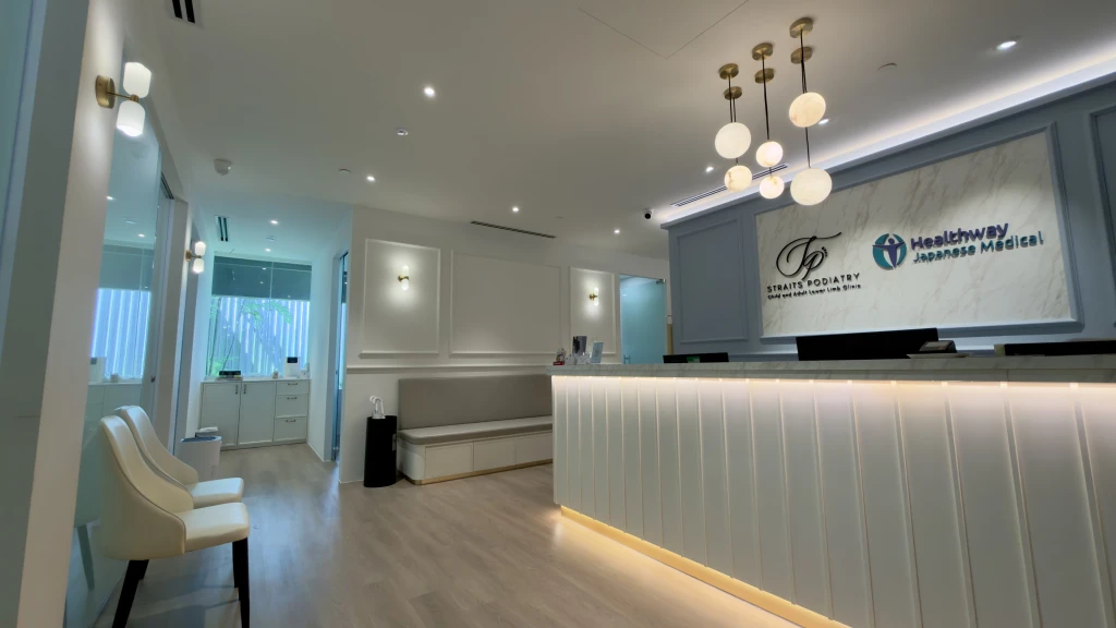 Interior of the Straits Podiatry Orchard clinic reception with a marble counter, Straits Podiatry and Healthway Japanese Medical signage, and pendant lights