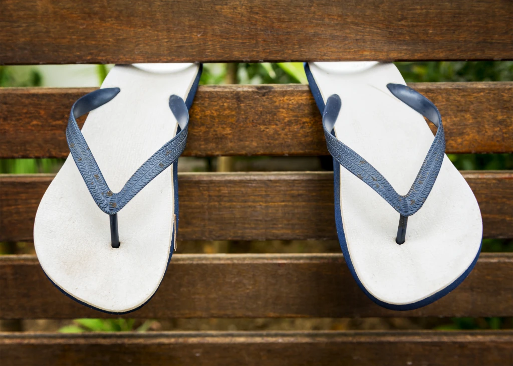 A pair of flat rubber flip flops resting on a wooden bench, the unsupportive thong style people often replace when looking for the best sandals for plantar fasciitis.