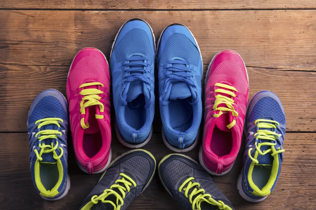 Six pairs of mesh running shoes in pink, blue and grey arranged on a wooden floor, the sort of line-up to compare when choosing what shoes to wear for plantar fasciitis.