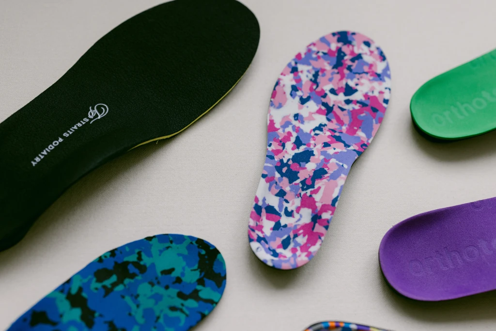 A flat lay of a black custom orthotic beside several coloured foam insole blanks, the arch support options behind the question should flat feet wear arch support