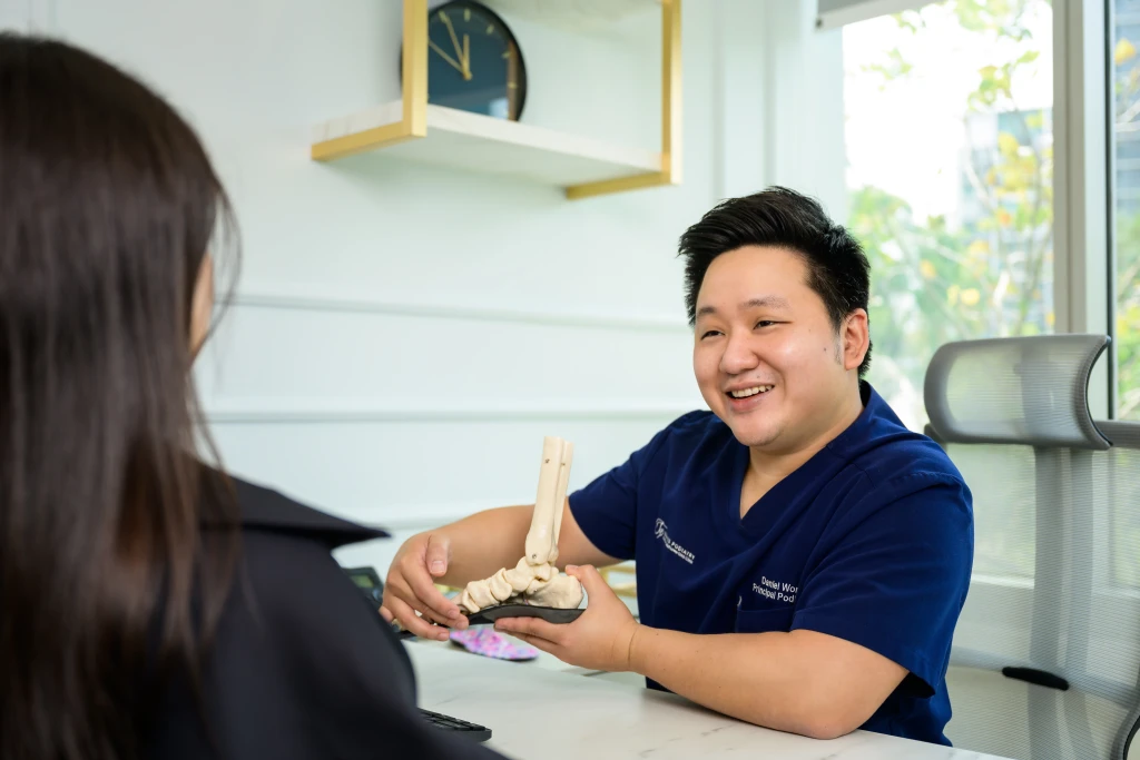 A podiatrist explains a foot skeleton model mounted on an orthotic insole to a patient across a desk, the consultation quality that matters in how to choose a podiatry clinic