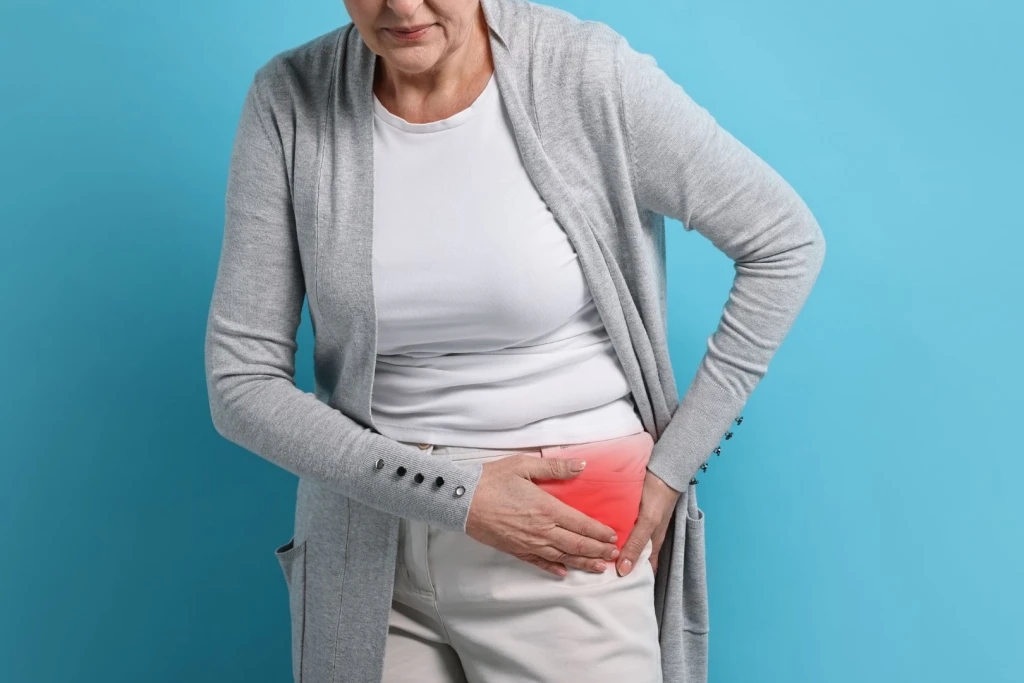 Middle-aged woman holding her left hip with both hands due to hip pain.