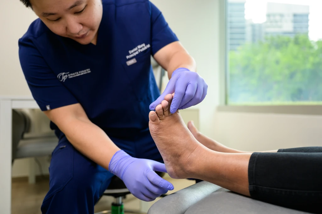 A podiatrist at Straits Podiatry examining a patient's heel during a clinical assessment.