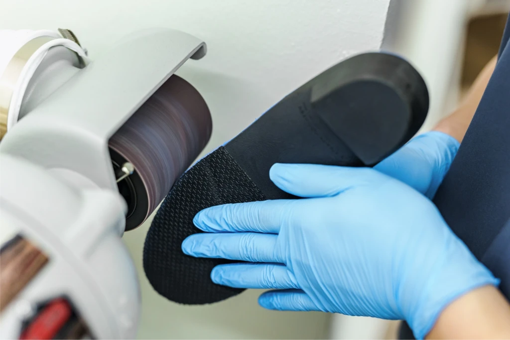 Straits Podiatry podiatrist shaping a custom foot orthotic on a grinding wheel in Singapore
