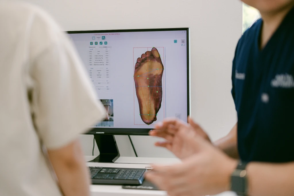 A 3D foot scan and its measurements shown on screen during a biomechanical assessment
