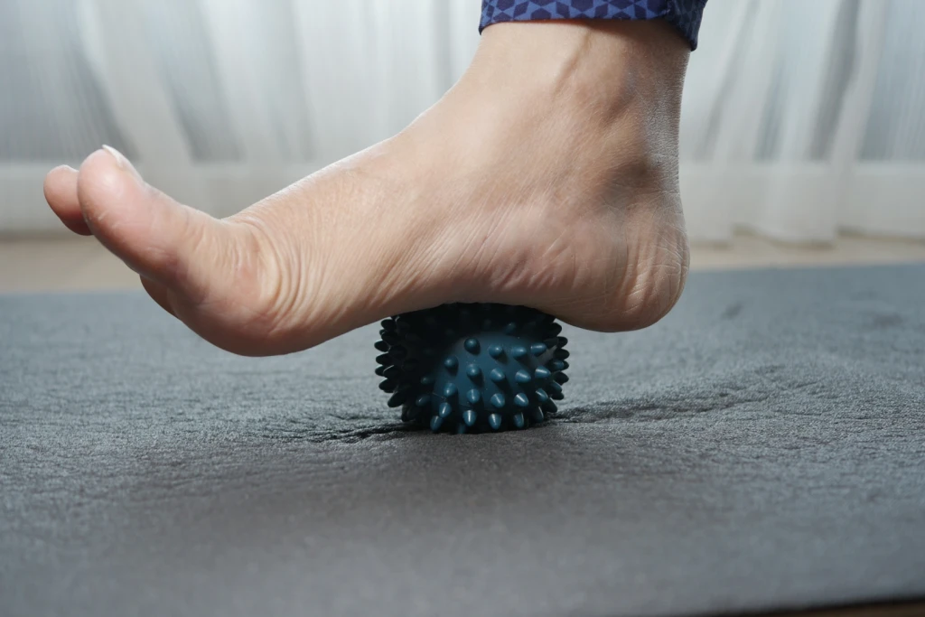 A bare foot rolling the arch over a spiky massage ball on a mat, a safe self-massage technique for plantar fasciitis