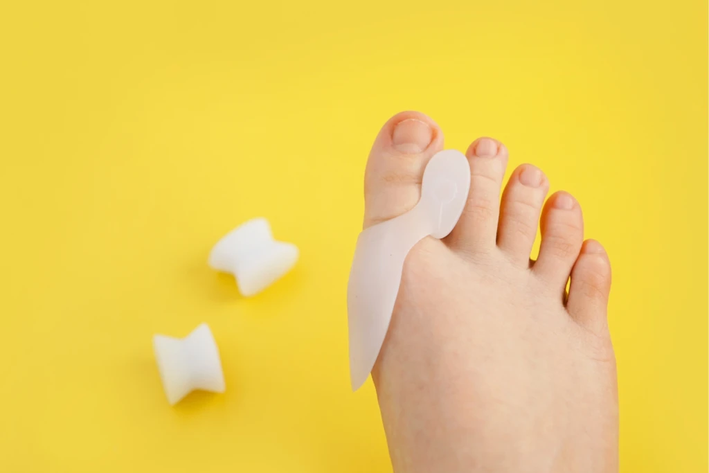 A gel bunion sleeve worn over the big toe joint beside two toe separators, on a yellow background