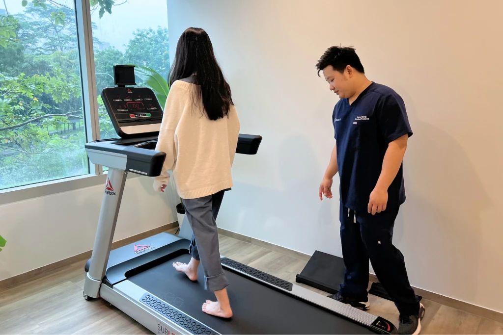 A podiatrist observing a patient walk barefoot on a treadmill during a gait assessment for ankle instability
