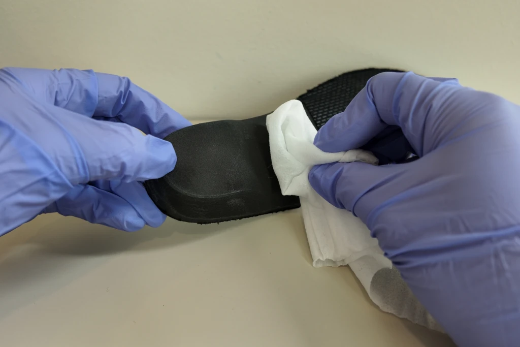 Gloved hands wiping a black custom insole clean with a wipe to maintain it and extend its life