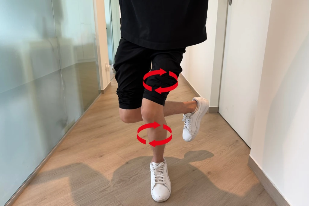A person performing a single-leg squat during assessment, with red arrows over the thigh and shin showing the leg rotating inward