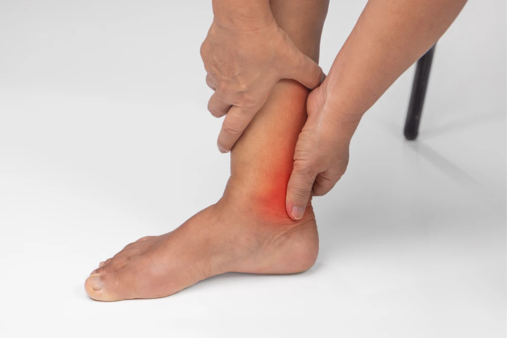 A person clutching the inner side of their ankle, with the sore area behind the ankle bone glowing red, over the posterior tibial tendon