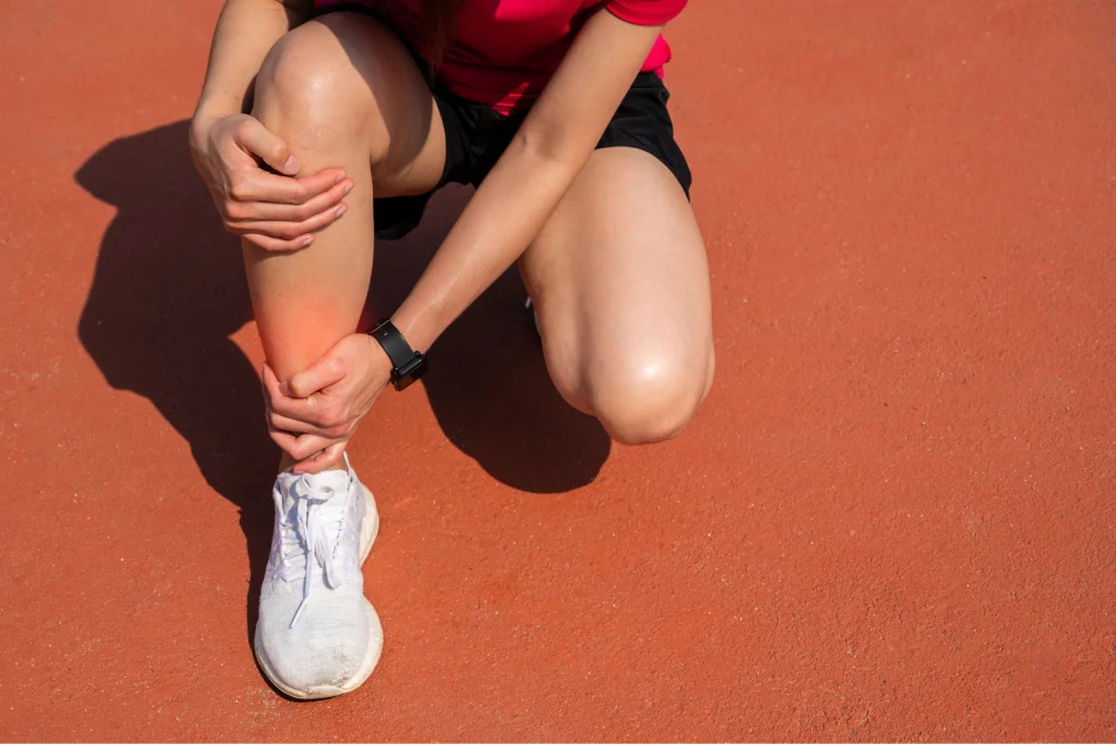 A runner crouched on a track, clutching her lower shin where a red glow marks shin splint pain