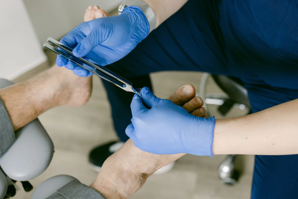 A gloved podiatrist holding a vibrating tuning fork against a patient's big toe to test sensation in the foot